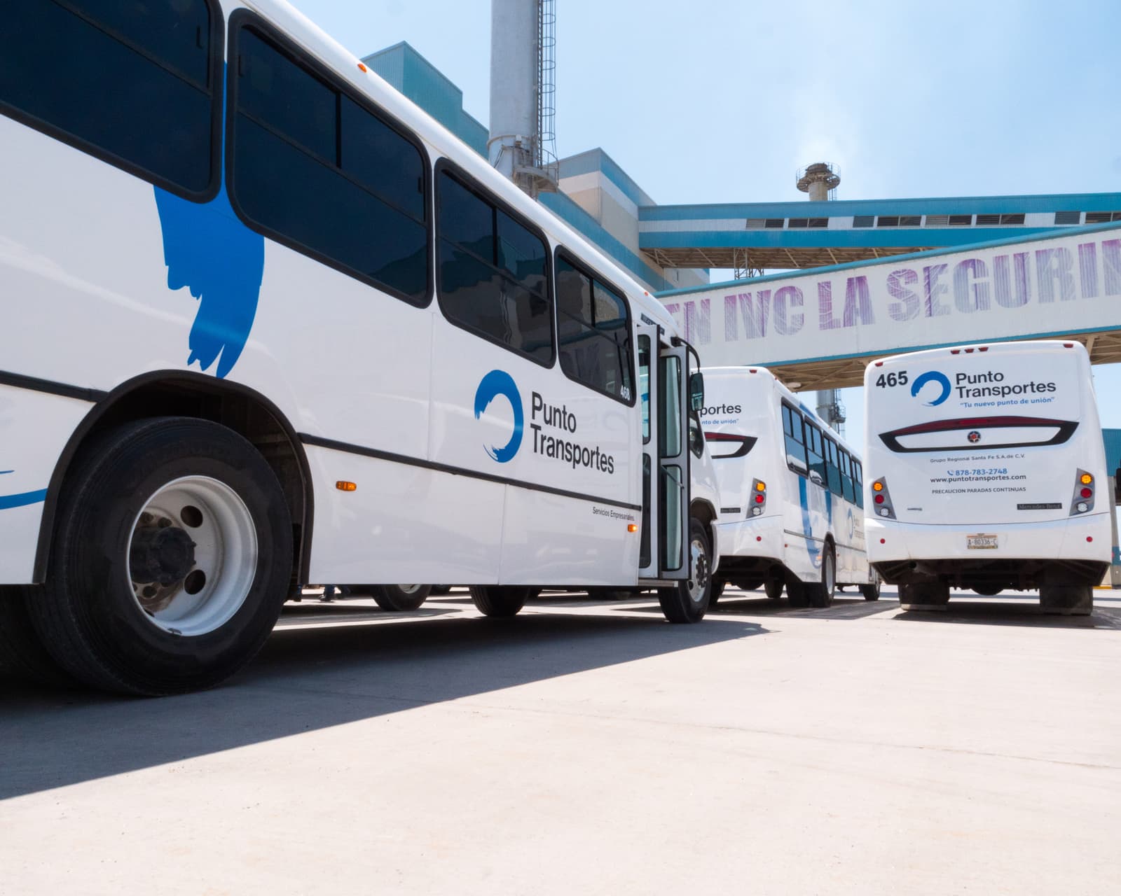 Fila de autobuses de Punto Transportes estacionados frente a una planta industrial